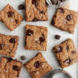 Top view of 8 scattered paleo blondies chocolate chip cookie bars on a white background
