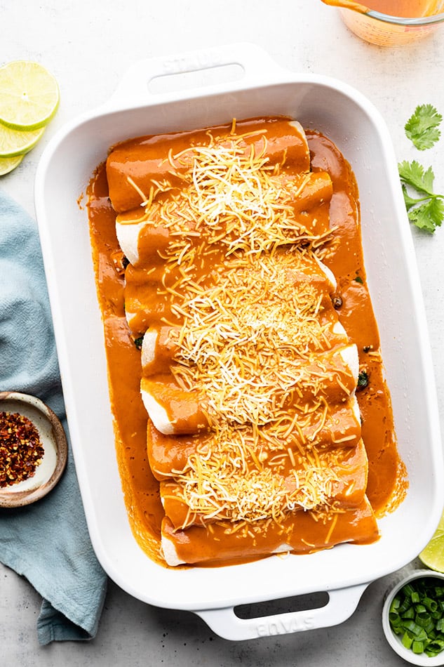 The fully assembled veggie enchiladas inside of a large white casserole dish before they've been baked