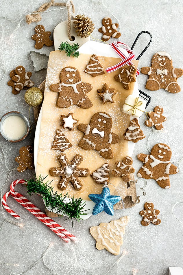 Top view of decorated vegan gingerbread cookies on a wooden cutting board on a grey background with cookie cutters