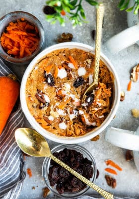 Top view of keto carrot mug cake in a white mug with a bit missing and a gold spoon on a grey background