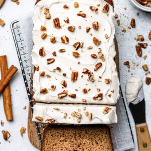 Top shot of a frosted gingerbread loaf with one slice on a wired rack