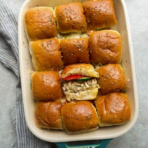 Top view of a dozen Buffalo Chicken Sliders in a rectangular dish with an open-faced sandwich