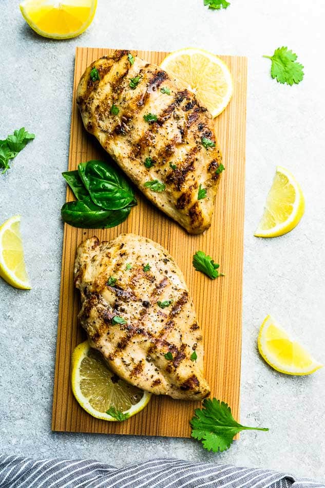 Two Grilled Chicken Breasts on a Wooden Cutting Board with Fresh Lemon Slices