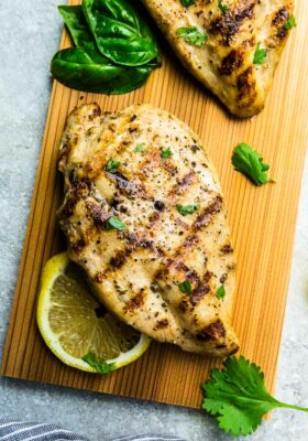 A Close-Up Shot of a Juicy Grilled Chicken Breast Beside Herbs and a Slice of Lemon