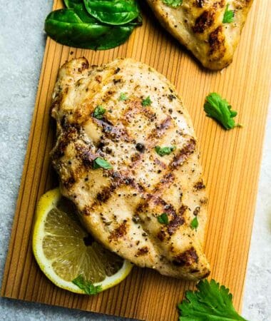 A Close-Up Shot of a Juicy Grilled Chicken Breast Beside Herbs and a Slice of Lemon