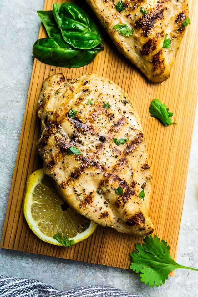 Top view of grilled chicken breast on a wooden cutting board on a grey background