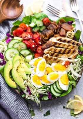 Top view of Cobb Salad with grilled chicken in a bowl on a grey background with lemon slices