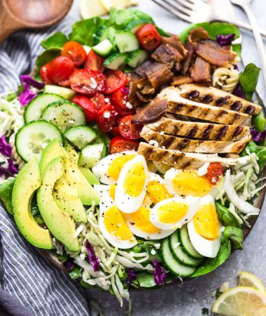 Top view of Cobb Salad with grilled chicken in a bowl on a grey background with lemon slices