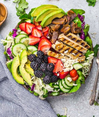 Top view of a loaded grilled chicken salad with berries in a bowl with two forks