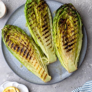 Overhead view of three grilled romaine heart halves on a grey plate