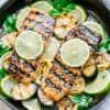 Top view of grilled salmon fillets in a cast iron pan with lime slices and zucchini