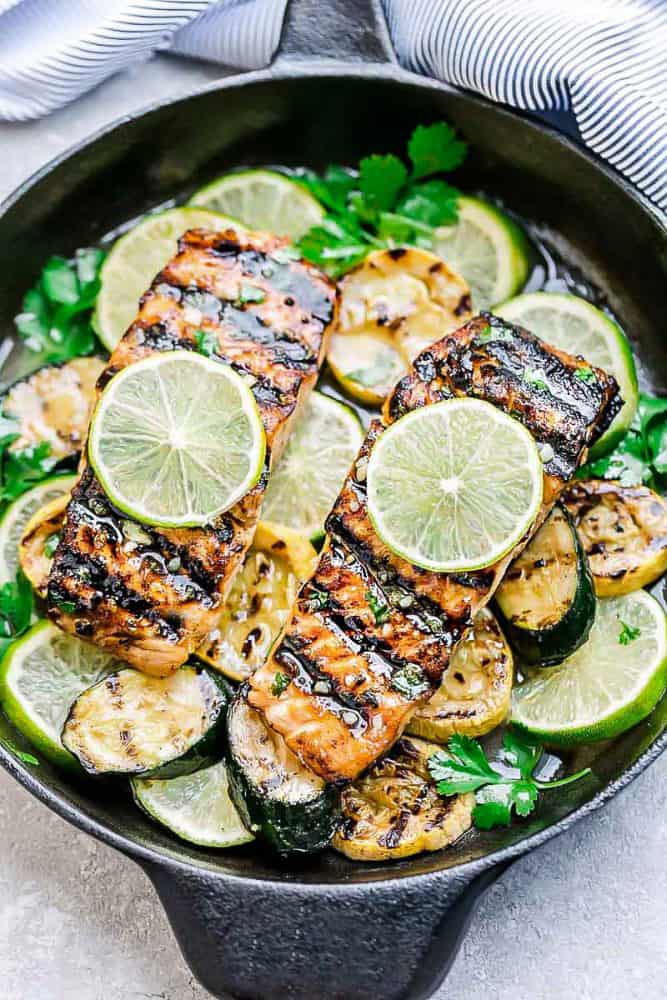 Top view of grilled salmon fillets in a cast iron pan with lime slices and zucchini