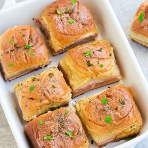 These Hot Oven Baked Ham and Cheese Sliders are the perfect game day snacks or appetizers. Best of all, they are a great way for using up any leftover ham from Thanksgiving, Christmas and Easter. Super easy to make with oven roasted ham, two cheeses and buttery garlic sauce over Hawaiian rolls. Great for feeding a crowd for a party or game day! #gameday #sliders #ham #cheese #swiss #cheddar #snacks #appetizer