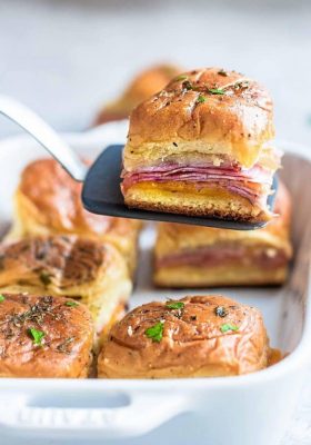 Spatula with a ham and cheese slider over a pan of buns