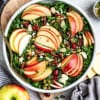 Top view of harvest kale salad with sliced apples in a white bowl