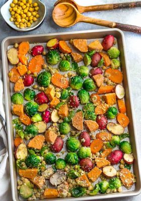 Flat lay of chopped roasted sweet potatoes, potatoes, Brussels sprouts, carrots and seasonings on a large baking sheet.