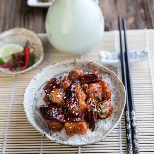 A bowl of General Tso's Chicken over white rice in a bowl next to chopsticks