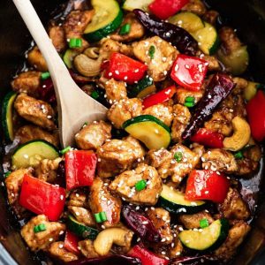 Close up of Slow Cooker Kung Pao Chicken with a wooden spoon in a crock pot