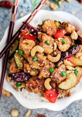 Kung Pao Chicken Stir Fry on a bed of white rice in a small white bowl with wooden chopsticks.
