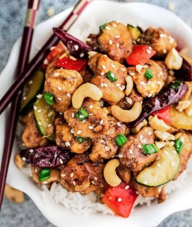 Kung Pao Chicken Stir Fry on a bed of white rice in a small white bowl with wooden chopsticks.