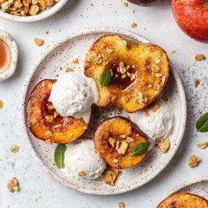 Overhead view of air fried fruit halves on a plate topped with granola and vanilla ice cream