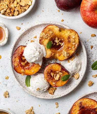 Overhead view of air fried fruit halves on a plate topped with granola and vanilla ice cream