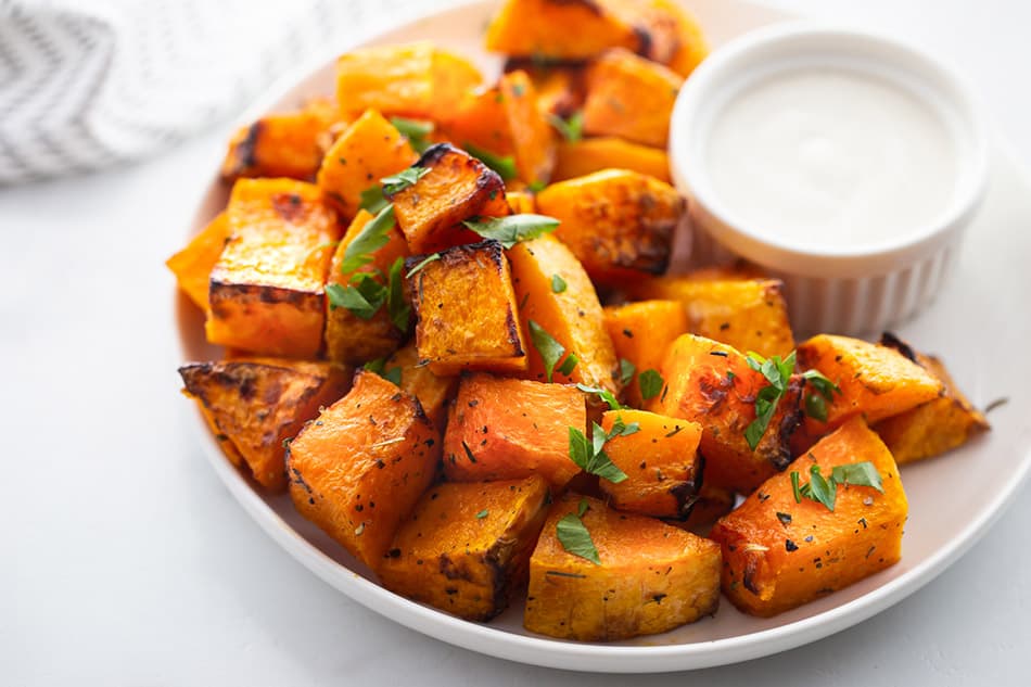 Roasted cubes of butternut squash on a plate with a garnish of chopped parsley