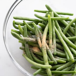 A bunch of raw green beans in a bowl with salt and pepper dumped on top of them