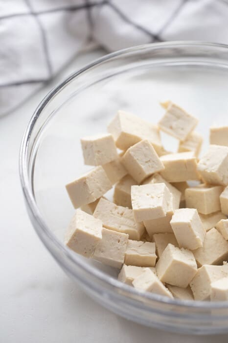 Side shot of raw tofu cubes in a clear mixing bowl