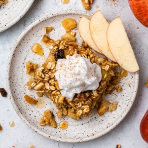 Top view of a square of vegan apple cinnamon baked oatmeal on a white plate with a dollop of vegan yogurt