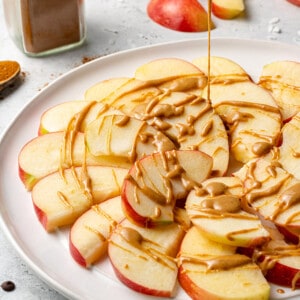 Nut butter being drizzled over apple slices on a plate