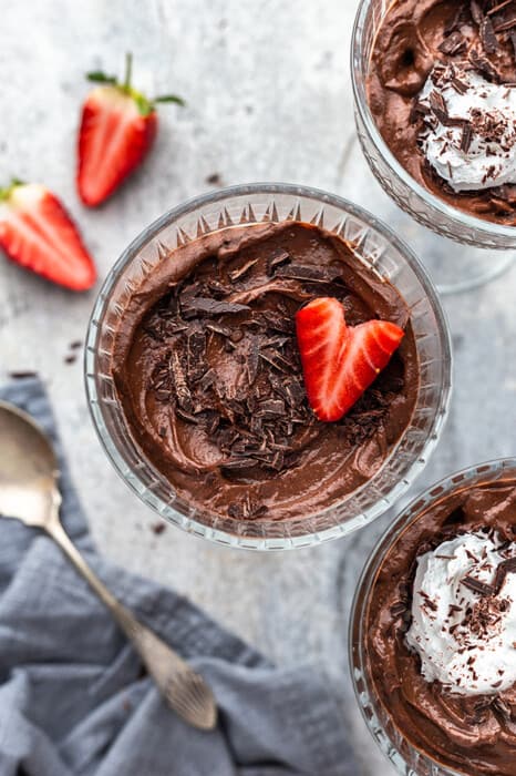 Avocado Chocolate Pudding in three glass jars with a strawberry