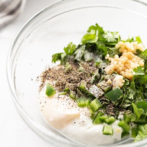 Chopped jalapeño, cilantro, minced garlic, dairy-free Greek yogurt and vegan mayo in a clear mixing bowl
