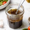Side view of balsamic vinaigrette dressing in a small jar with a spoon