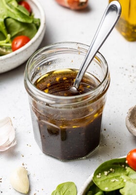 Side view of balsamic vinaigrette dressing in a small jar with a spoon