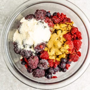 Top view of mixed berries tossed with arrowroot starch and coconut sugar in a clear bowl