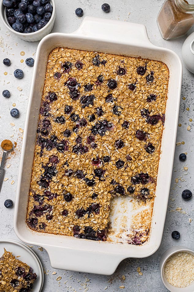 A baking dish full of blueberry baked oatmeal with one serving missing from the pan