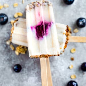 Top view of three vegan blueberry popsicles stacked on a grey blue background with blueberries on the side