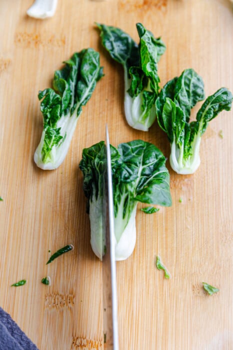 Four bok choy bunches on a wooden cutting board with a knife