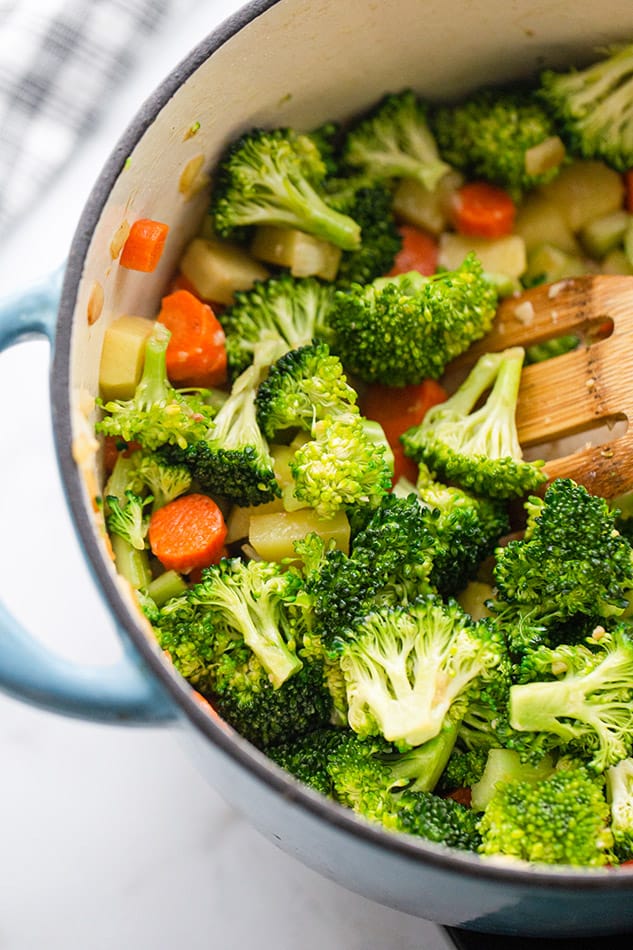 A pile of fresh carrots, broccoli, celery and potatoes in a dutch oven pot