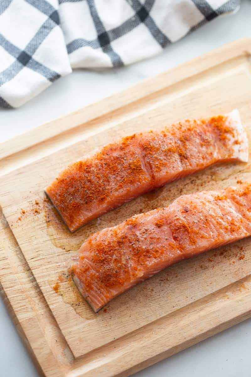 Two uncooked seasoned salmon fillets on a wooden cutting board