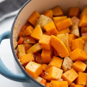 Cooked butternut squash cubes, carrots and apples in a blue dutch oven pot