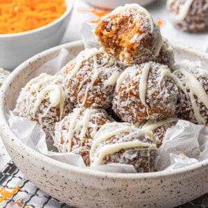 Side view of a stack of carrot cake bliss balls with a missing bite in a white bowl