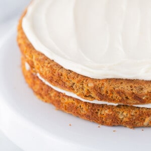 45 degree shot of two layers of gluten free carrot cake with frosting on a white cake platter