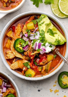A close-up image of a bowl of chicken tortilla soup topped with avocado slices and dairy-free sour cream