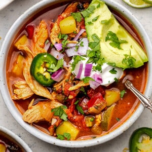 A close-up image of a bowl of chicken tortilla soup topped with avocado slices and dairy-free sour cream