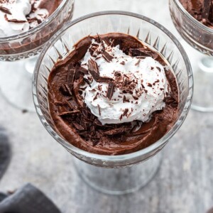 A serving of healthy chocolate mousse topped with whipped cream in a clear goblet.