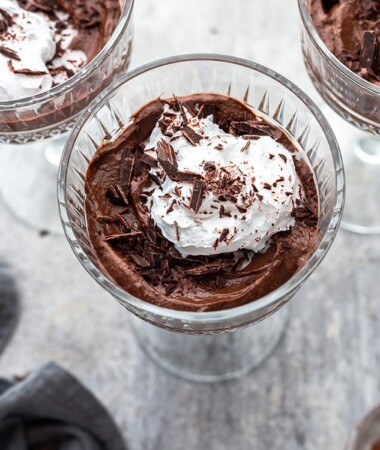 A serving of healthy chocolate mousse topped with whipped cream in a clear goblet.