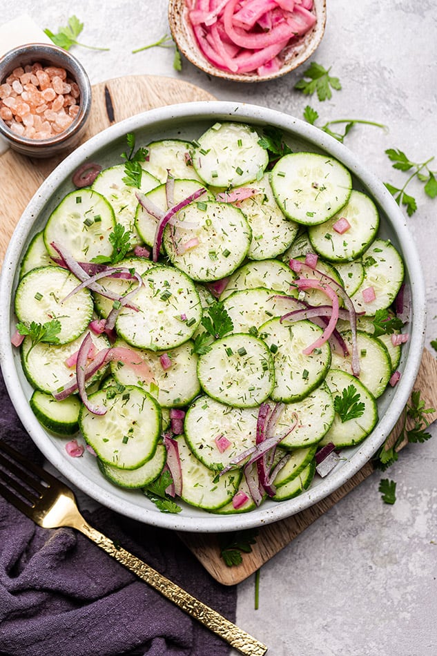 Top view of fresh cucumber salad in a white bowl with a gold fork