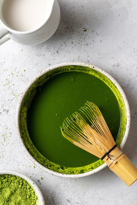 Whisked matcha powder in a white bowl with a bamboo whisk